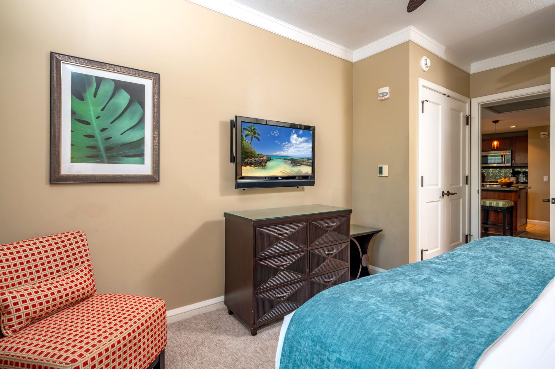 This guest room includes a wall-mounted TV, cozy reading chair, and easy access to the kitchen and living area for added comfort and convenience.