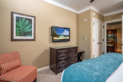 This guest room includes a wall-mounted TV, cozy reading chair, and easy access to the kitchen and living area for added comfort and convenience. HKH-520