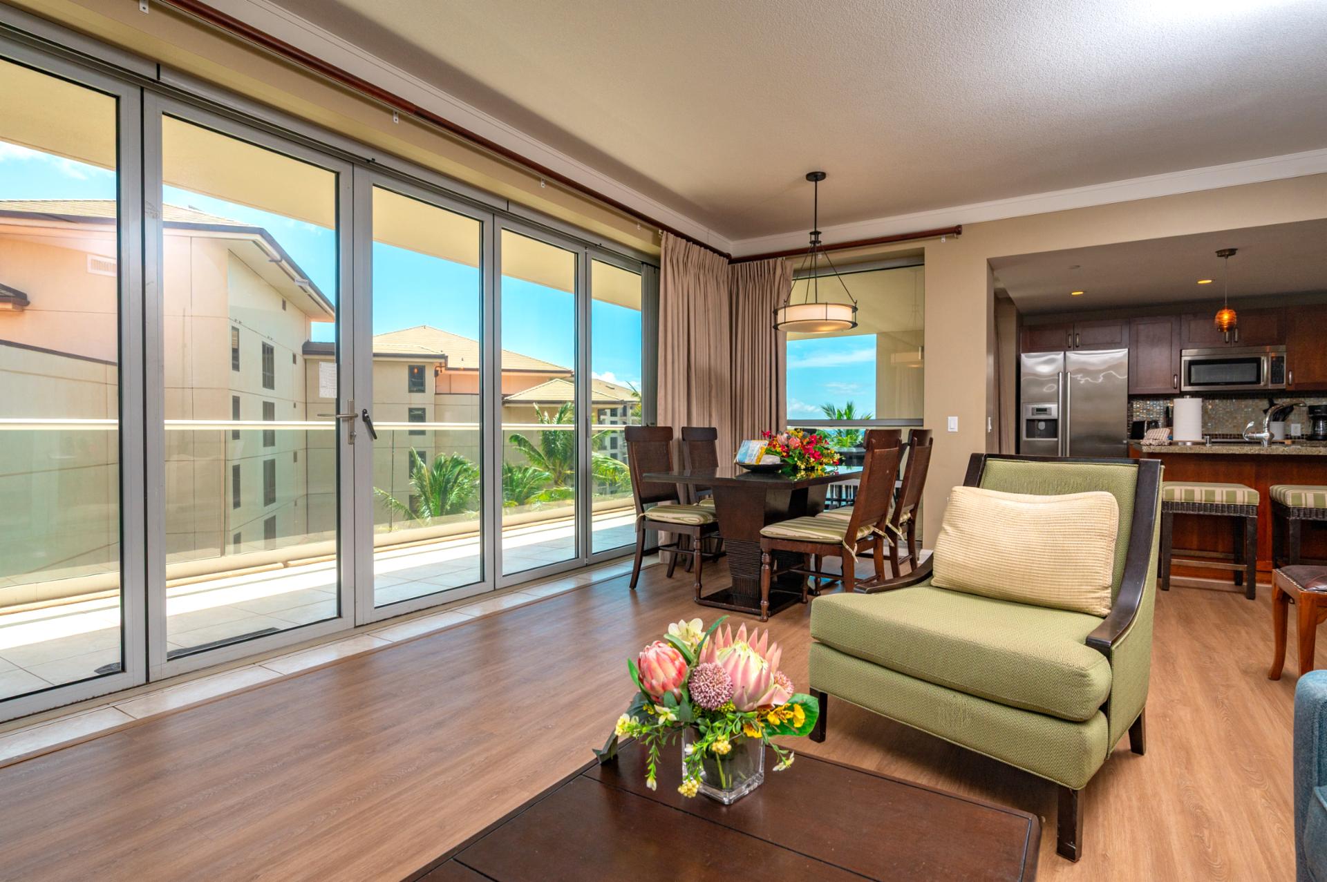Natural light pours into the open living and dining area through full-length glass doors, inviting you to step out to the wraparound lanai.