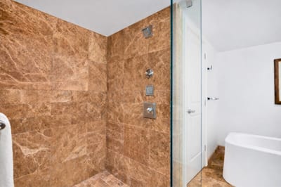 Glass-enclosed walk-in shower with stone accents and rainfall head. HKH-550