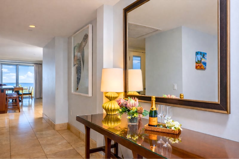 Ocean-view entry hallway at Honua Kai Hokulani 550 — sea turtle artwork, a welcome console with champagne service, and a glimpse of the Pacific through the living room lanai doors
