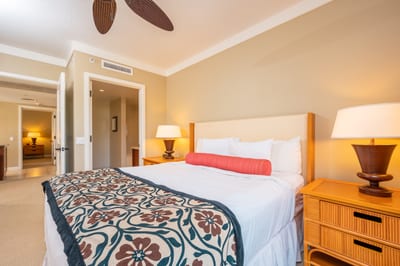 Tropical-style bedroom with plush bedding, warm lighting, and ensuite access.