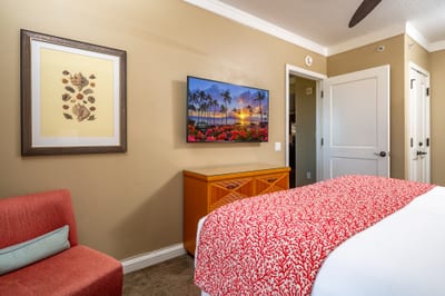 The primary bedroom features tropical island decor with a pop of red color