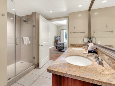 Modern bathroom with glass shower, granite counter, and bedroom access.