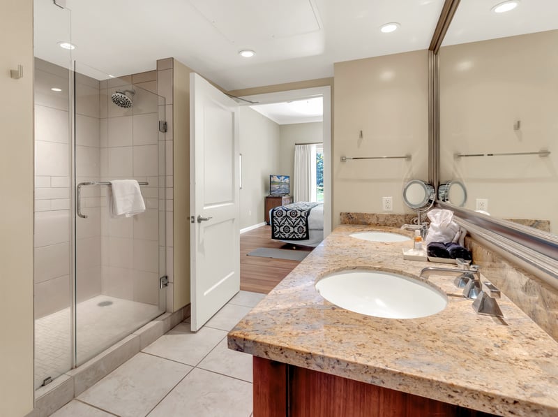 Modern bathroom with glass shower, granite counter, and bedroom access.