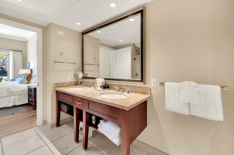Elegant bathroom with double sinks and view into cozy bedroom.