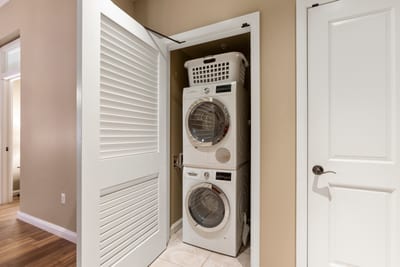 Compact laundry closet with modern stacked washer, dryer, and basket.