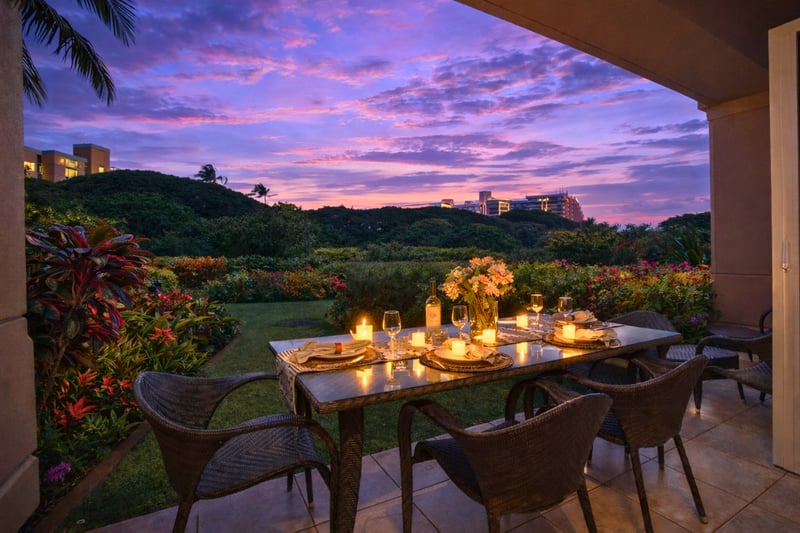 Dine al fresco on your private lanai as sunset colors glow over lush resort grounds and a hint of ocean beyond.