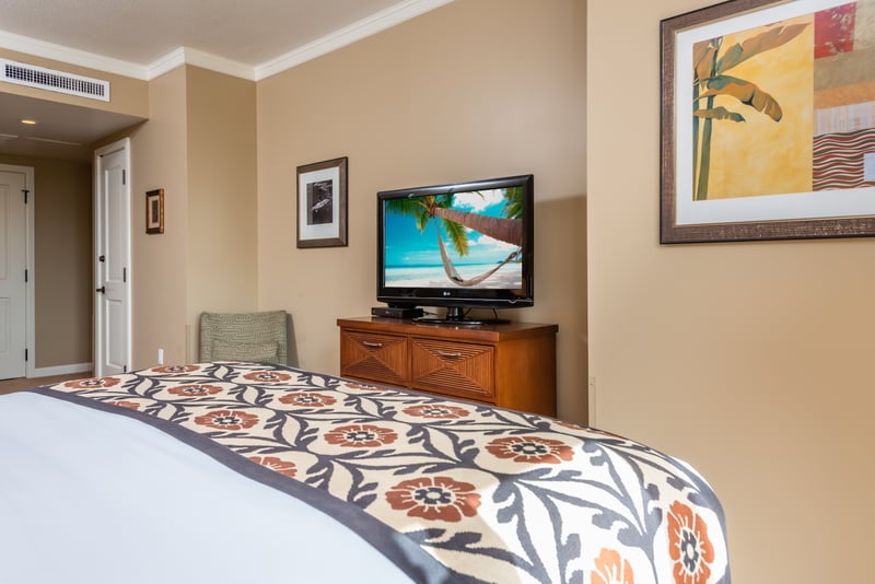 Comfortable bedroom with tropical decor, flat-screen TV, and warm tones. HKK-225