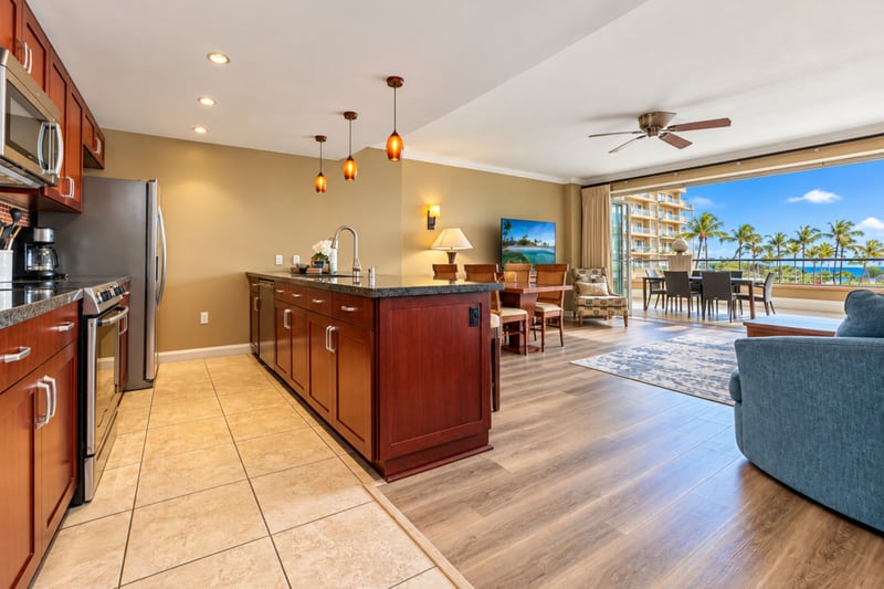 Your open kitchen flows into the dining and living areas, where Nano glass doors open to the lanai and ocean views beyond the palms. HKK-229