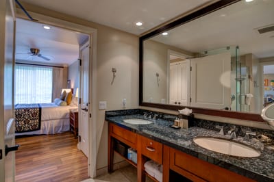 Spacious bathroom with double sinks opens to serene tropical bedroom.