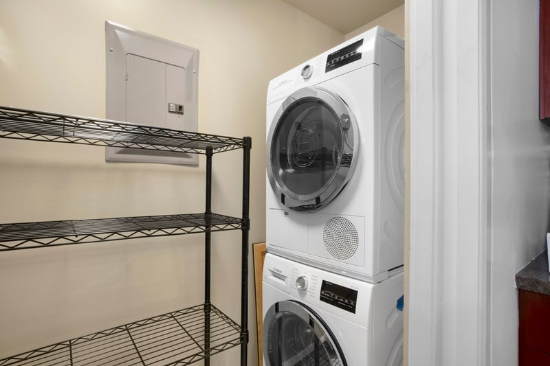 Convenient laundry room with modern stacked washer, dryer, and shelving.