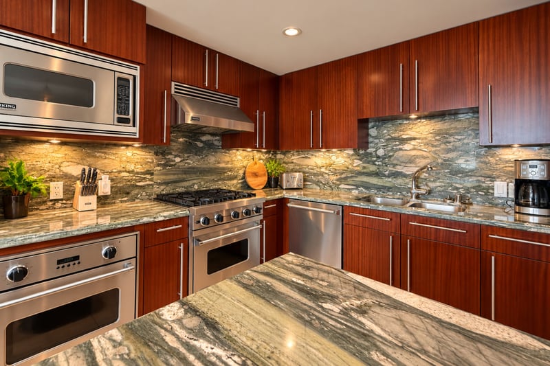 A microwave, built in oven and dishwasher sit within easy reach, with warm lighting along the stone countertops.