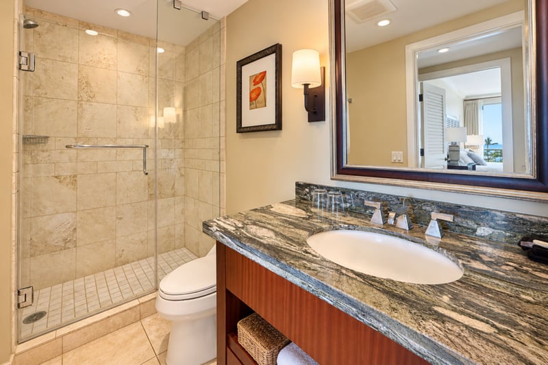 A glass enclosed tile shower and a stone topped vanity with a framed mirror make this bathroom easy to use.