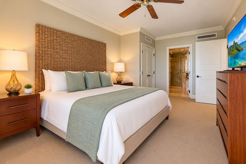 A second view of the master bedroom shows the king bed, a ceiling fan, a dresser with television and an open doorway to the bathroom.