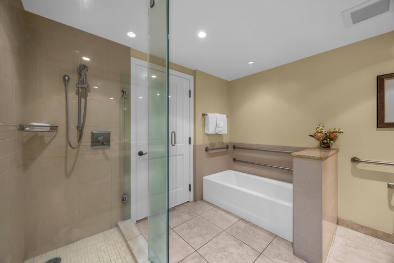 ADA-accessible bathroom at Honua Kai Konea 524 with a glass-enclosed walk-in shower, grab bars, and a separate soaking tub.