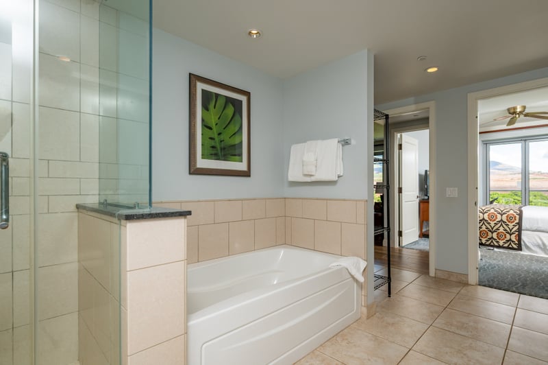 Primary bathroom at Honua Kai Konea 706 — soaking tub, glass-enclosed shower, and a view through to the bedroom