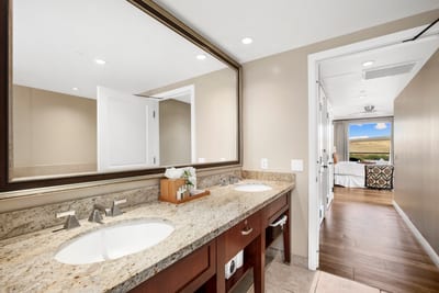 Spacious bathroom with double sinks and scenic bedroom view beyond.