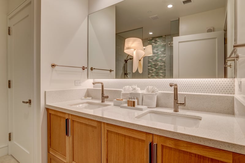 Double-sink vanity with quartz countertop, undermount sinks, and a well-lit mirror opening to the walk-in shower.