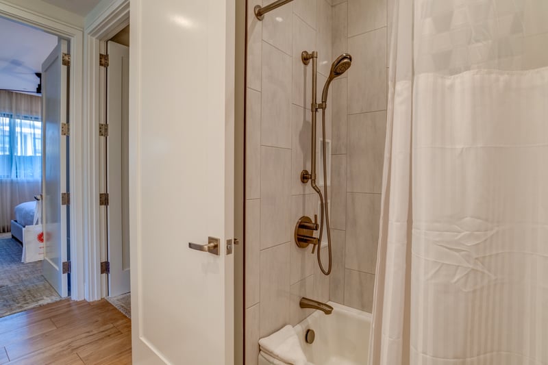 Bathroom with tiled tub-and-shower combo, brushed-bronze fixtures, and a rain-style handheld showerhead.