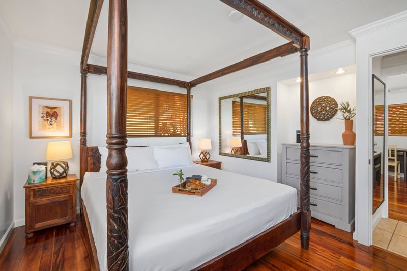 A bed fit for island royalty stands beneath wooden beams, surrounded by cozy lighting and jungle-kissed windows