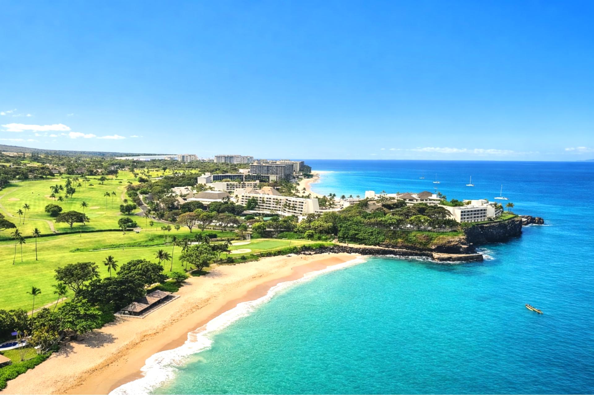 A breathtaking aerial view of Ka’anapali Beach glows under the setting sun, where lush fairways meet tranquil turquoise waters and luxury resorts line the coast in perfect harmony.