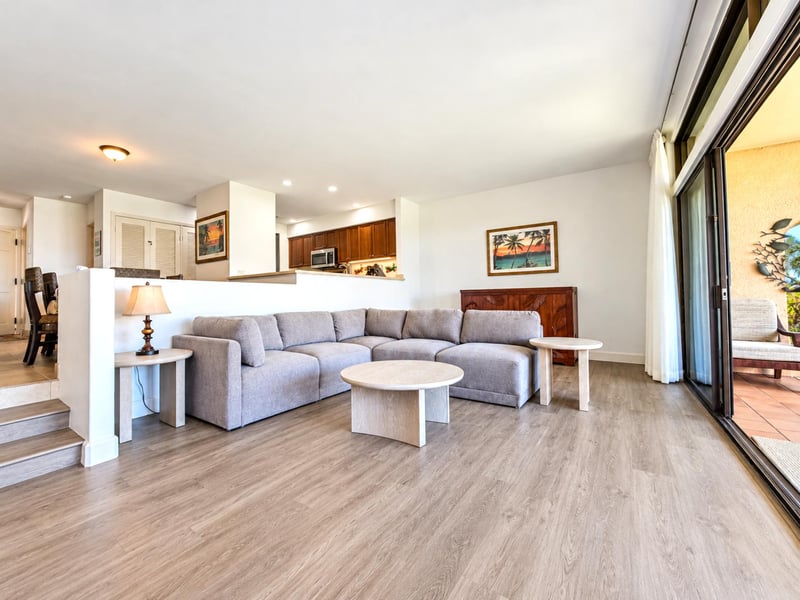 A gray sectional sofa and round, light coffee tables anchor your living room, with the kitchen just a few steps up beyond.