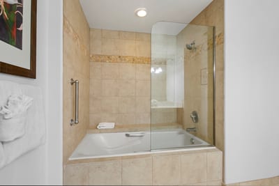 Encased in frameless glass, the deep soaking tub is wrapped in creamy tile and crowned with a mosaic band for subtle charm