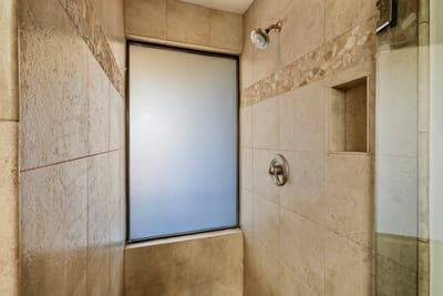 Wrapped in creamy stone tile, the walk-in shower is accented by a mosaic trim and a frosted window for diffused daylight