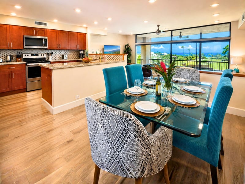 A glass top table set with wine glasses and place settings sits open to the kitchen, ready for a shared meal with a view.