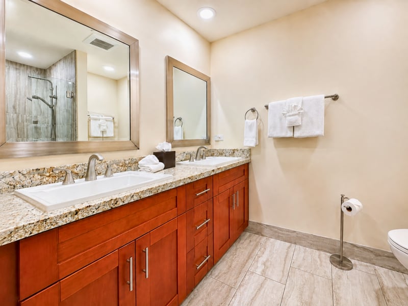 Twin sinks are set into a shell inlaid granite counter in the ensuite guest bath, with the mirrors reflecting the glass walk in shower beyond.