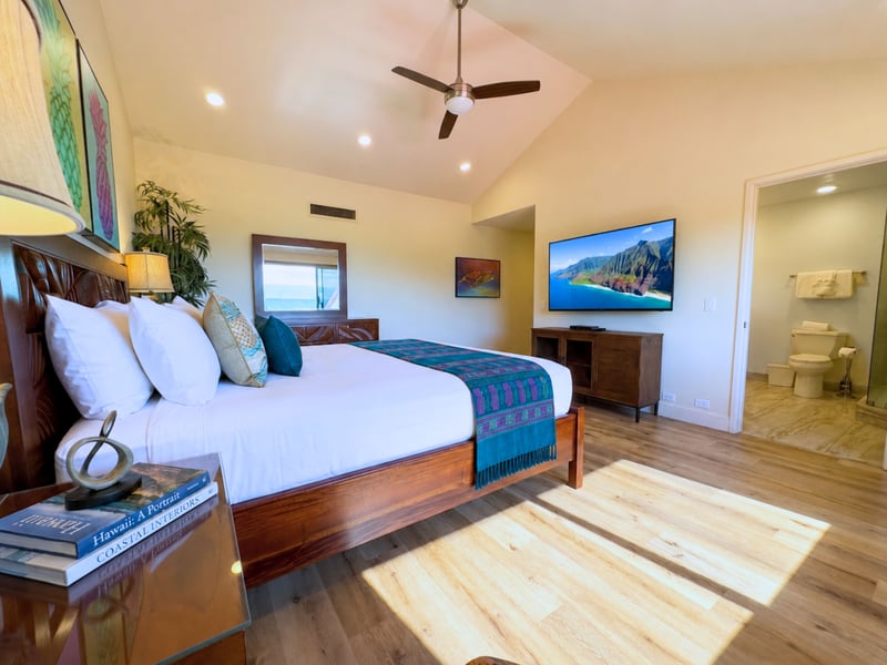 The primary bedroom looks through to its own ensuite bath, with a wall mounted television and artwork bringing in island color.