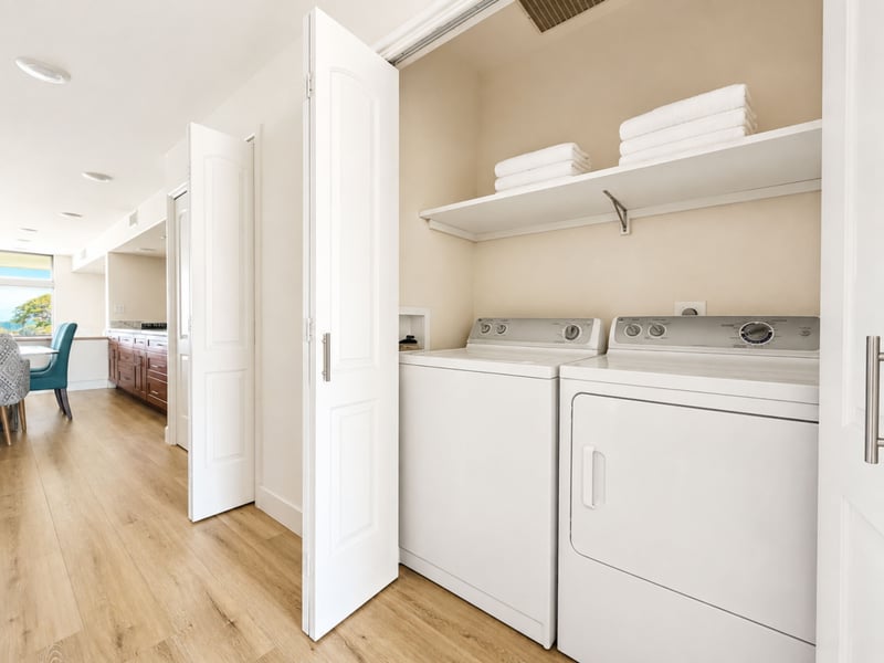 A full size washer and dryer sit ready in the laundry closet, with fresh folded towels stacked on the shelf above.