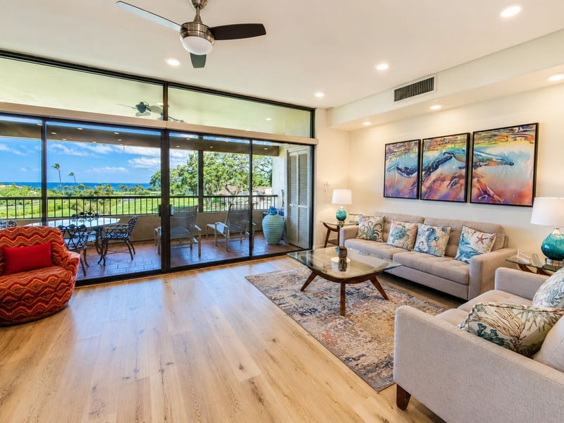 Living room at Kaanapali Royal P301 - a vibrant whale triptych anchors the seating area, with floor to ceiling sliders opening to the private lanai for sweeping ocean and golf course views.