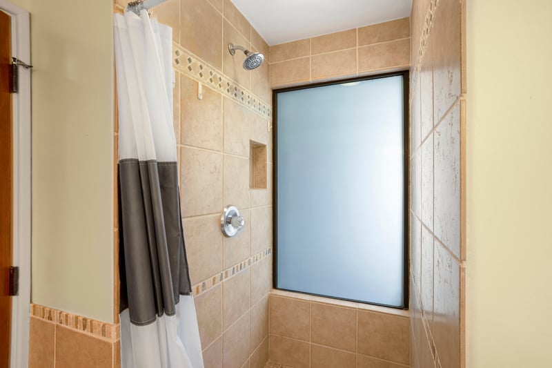 The shower-tub combo is surrounded by sun-kissed tile and features a frosted window that diffuses light with spa-like serenity