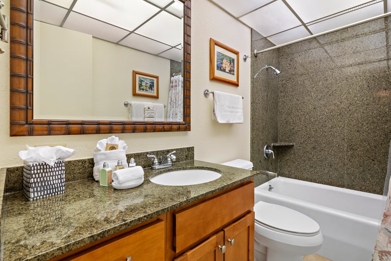 The tub-shower combination is wrapped in speckled stone tile, offering a clean-lined backdrop with earthy, coastal flair