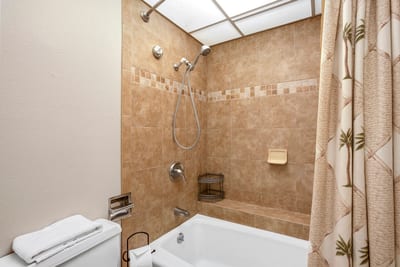 Wrapped in caramel-toned tile, the tub and shower ensemble features a mosaic border and palm-print curtain for a tropical nod
