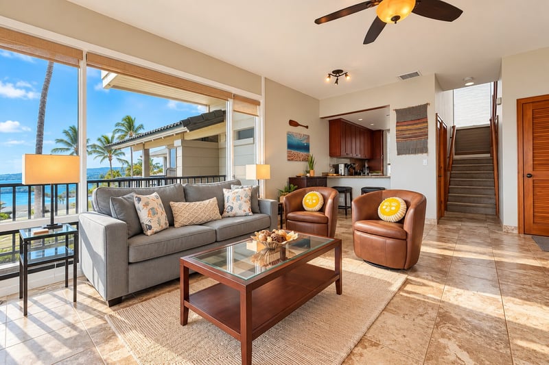Sunlit tile floors and a glass top coffee table anchor the seating area, with the kitchen bar and stairs just beyond. KBV-15B3