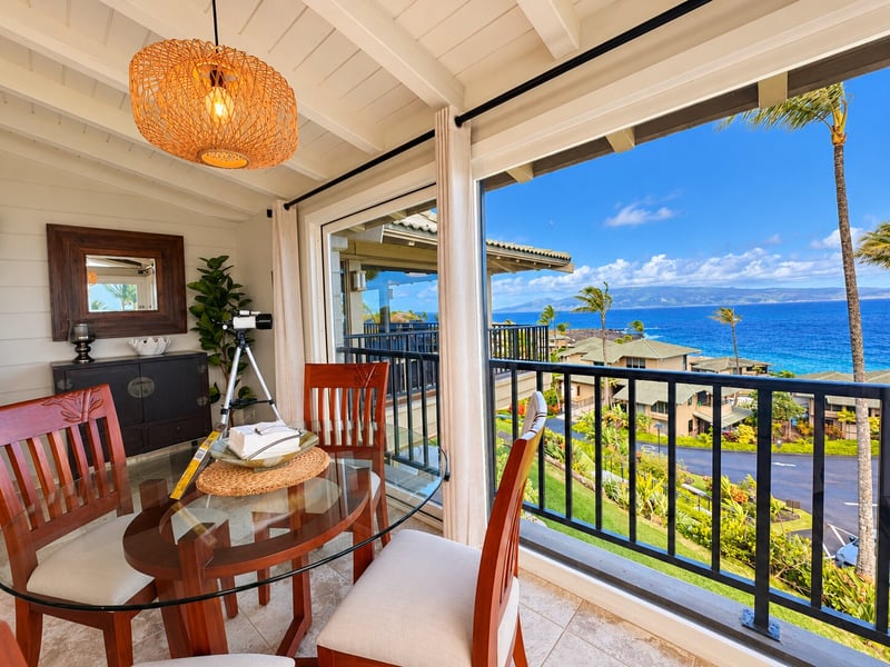 A beamed ceiling and woven pendant light add warmth over the dining table, with the balcony and ocean just outside the glass. KBV-15B3
