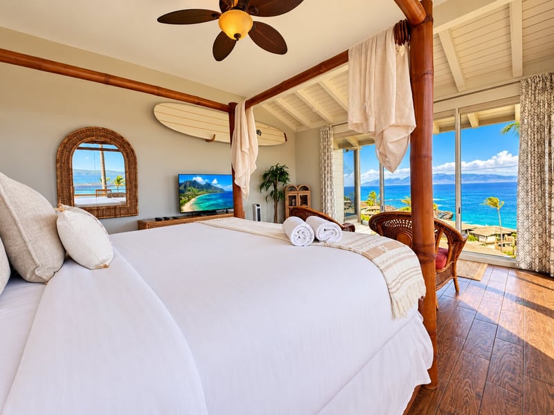 A wall-mounted surfboard, a mirror, and a television give the bedroom island character, with ocean views through the corner windows. KBV-15B3