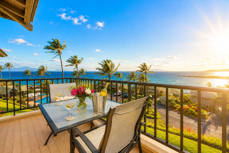 Your covered lanai holds a dining table for two, ideal for sunset drinks with the pool and coastline visible below.