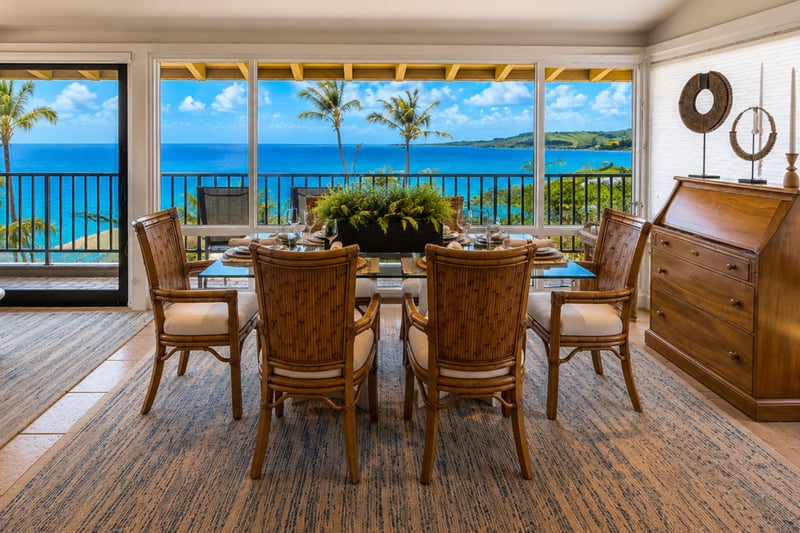 Your dining table seats six under a covered lanai, with sweeping ocean views stretching past the railing to the coastline.