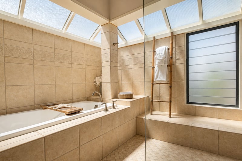 A deep soaking tub sits beneath a skylight in your primary bathroom, with a wood caddy for bath essentials within reach.