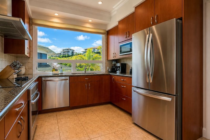 Your kitchen's window over the sink frames a lush hillside view, with stainless steel appliances, granite countertops, and rich wood cabinetry throughout.