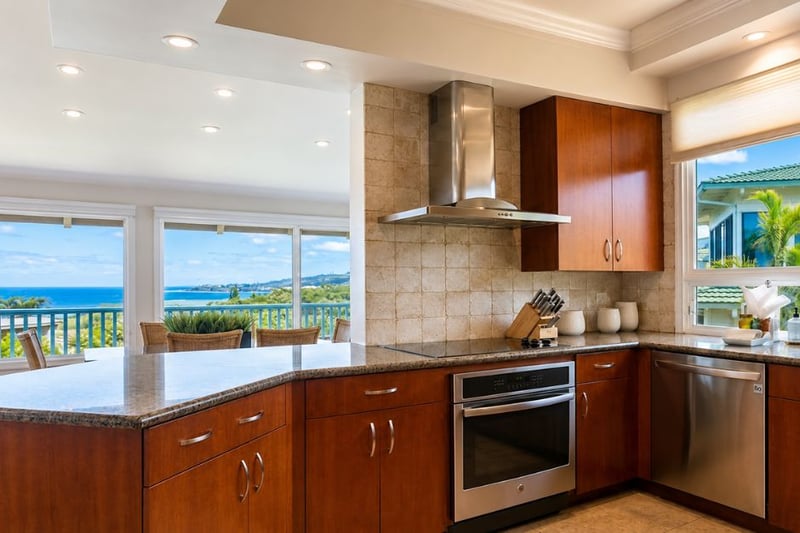 The kitchen's stone backsplash and stainless range hood sit steps from an ocean-view peninsula, connecting cooking and dining to the water beyond.