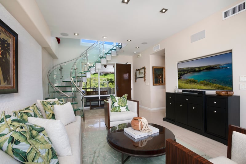 Elegant tropical-style living room with glass spiral staircase and views.