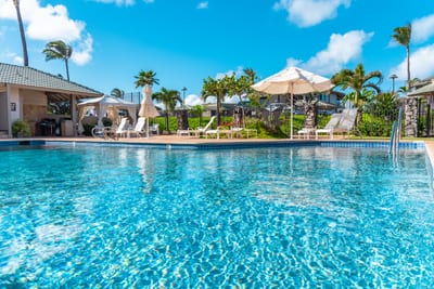 Sparkling resort pool surrounded by loungers, umbrellas, and tropical palms.