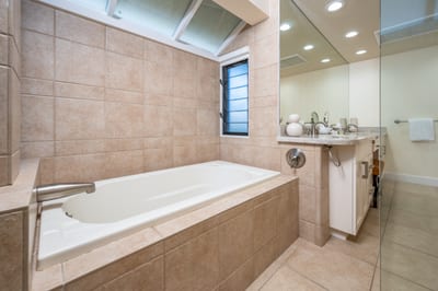 Step into comfort with a large mirror-lit vanity, tiled soaking tub, and calming neutral tones throughout