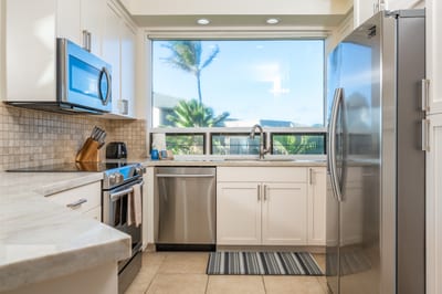 This sleek kitchen pairs clean white cabinetry with lush window views—culinary calm meets island color