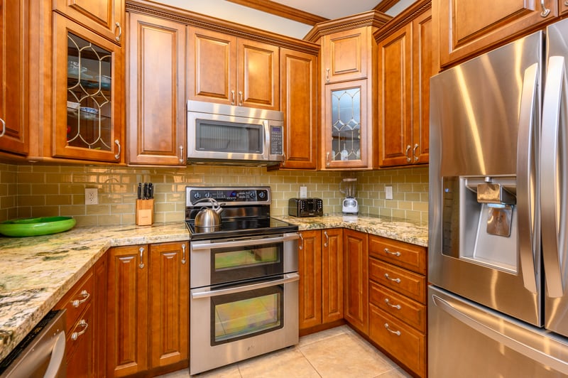 Modern kitchen with stainless appliances, granite counters, and warm cabinetry. KGV-16P3